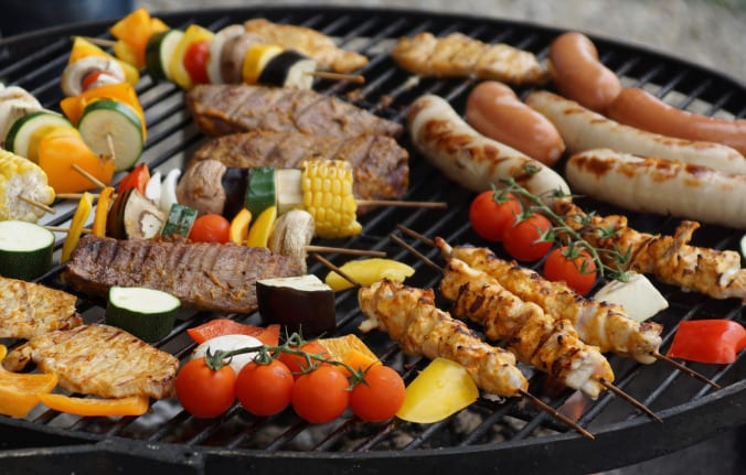 Vegetables, chicken, beef, and sausage over an outdoor grill